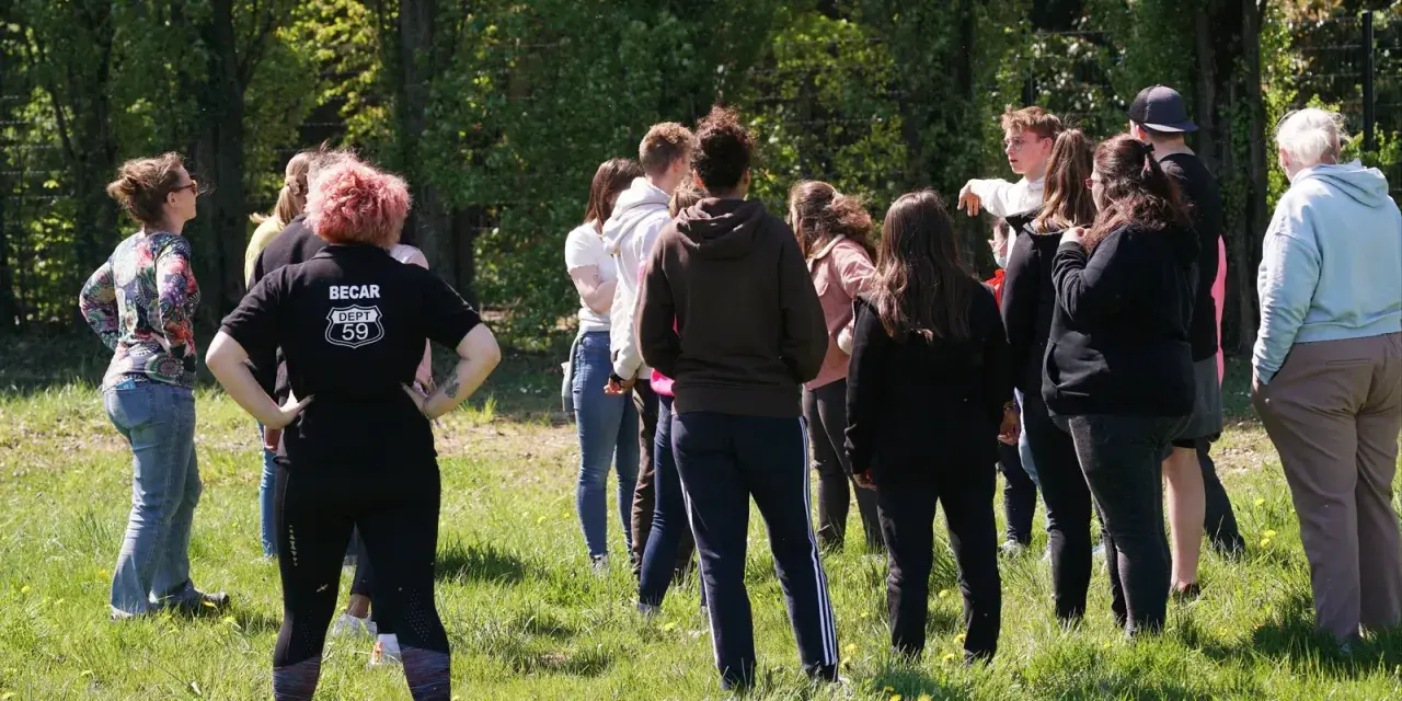 Groupe de jeunes adultes debout dans un champ verdoyant, certains se regardent.