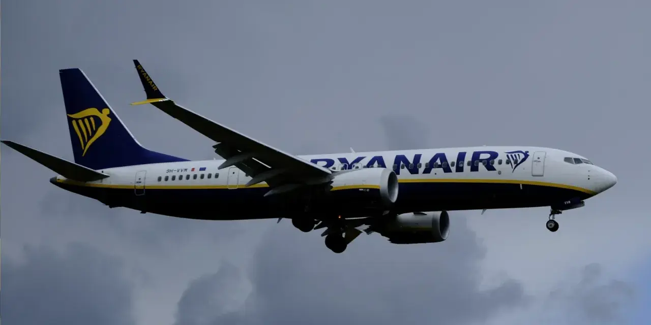 Samolot Ryanair z logo na ogonie leci na tle pochmurnego nieba. Może to być symbol zmiany nazwiska, gdy pasażerowie zmieniają swoje dane przed podróżą.