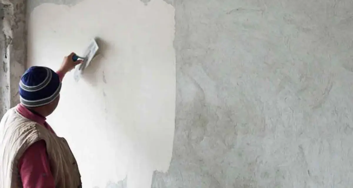 Un artisan applique un enduit chaux sable intérieur sur un mur avec une truelle. La texture naturelle du mortier est visible.
