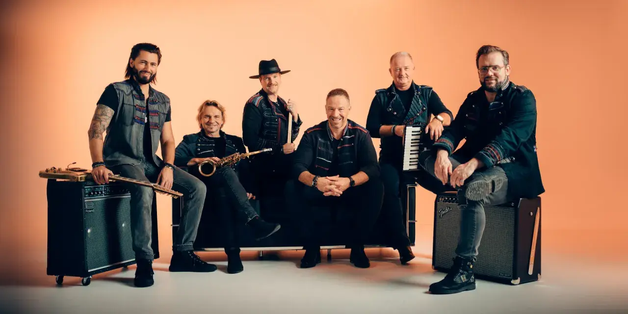 Sechs Männer einer Band posieren vor orangefarbenem Hintergrund, einige sitzen, einer steht.