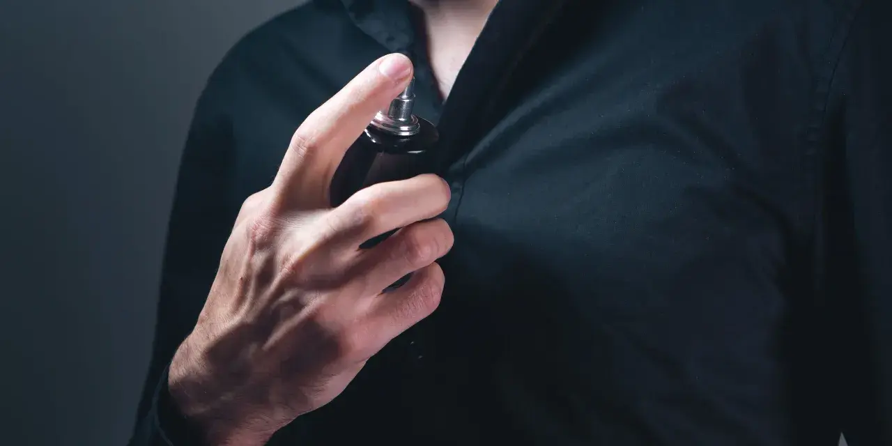 Mann sprüht sich Parfum auf die Brust.
