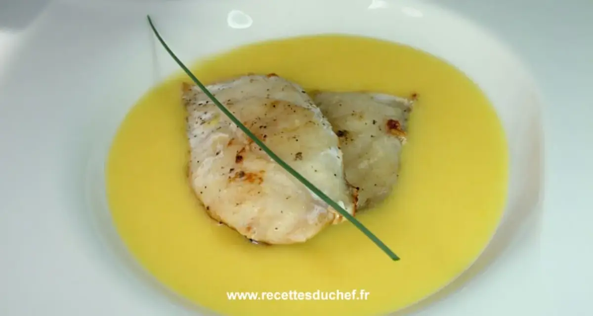 Deux filets de poisson poêlés reposent dans une onctueuse sauce à l'orange, décorés d'une tige de ciboulette.