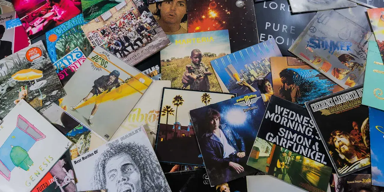 Eine bunte Sammlung von Schallplatten zeigt, welche Musikarten es gibt: Rock von AC/DC, Pop von Genesis, Folk von Simon & Garfunkel und Reggae von Bob Marley.