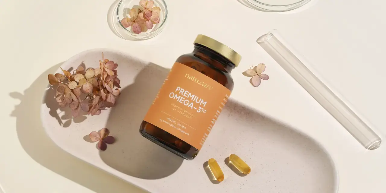 Suplement Omega-3 z DHA dla kobiet w ciąży, wspierający rozwój mózgu dziecka. Na zdjęciu buteleczka i kapsułki na tle suszonych kwiatów.