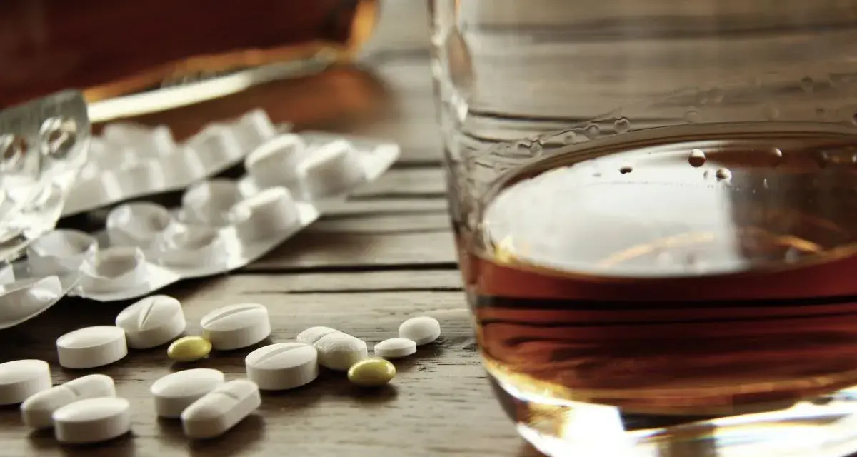 Tabletki i szklanka z alkoholem. Zastanawiasz się, po jakim czasie od zastrzyku można pić alkohol? To ważne pytanie.
