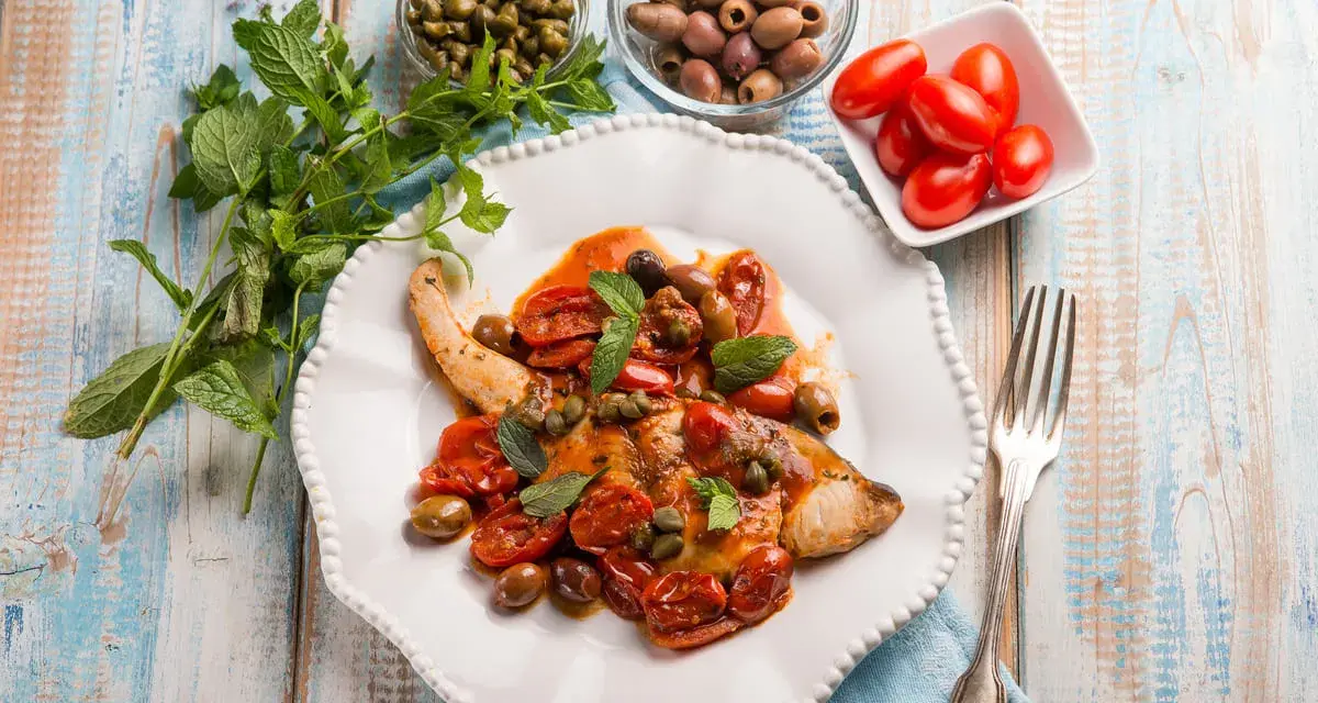 Un saporito pesce spada alla siciliana, condito con pomodorini, olive e capperi, guarnito con menta fresca.
