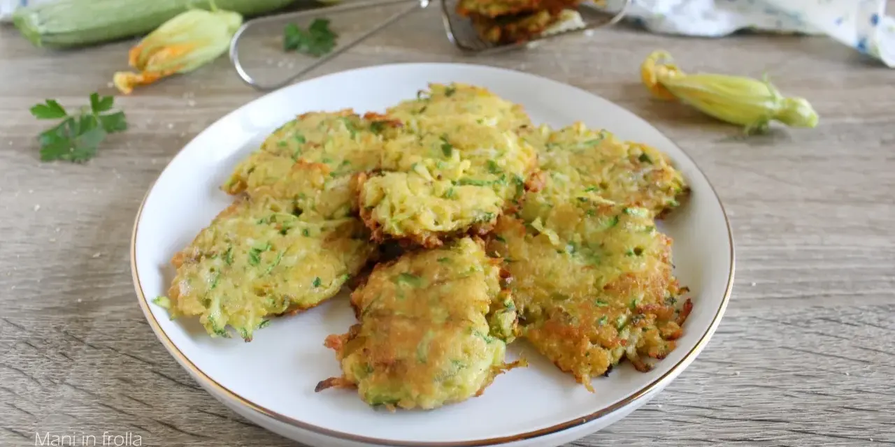 Buñuelos de calabacín dorados y crujientes en un plato blanco, con calabacines y flores en el fondo.