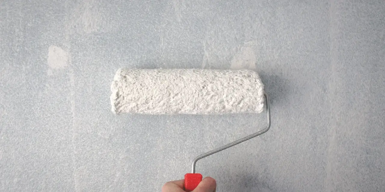 En hand håller en färgroller med vitt spackel för att jämna ut en tapet.