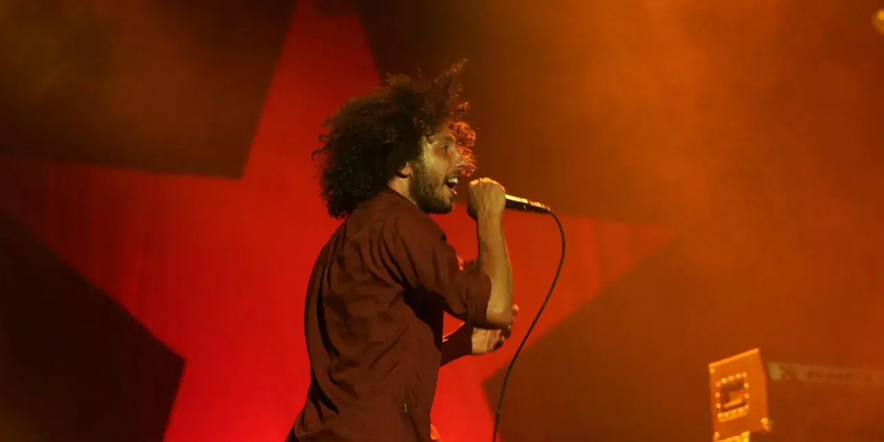 Zac Zack de la Rocha śpiewa z pasją na koncercie Rage Against the Machine. Czerwona gwiazda w tle podkreśla energię występu.