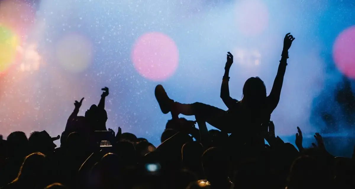 Tłum na jednym z największych festiwali muzycznych na świecie. Kobieta na rękach, ręce w górze, światła sceny.