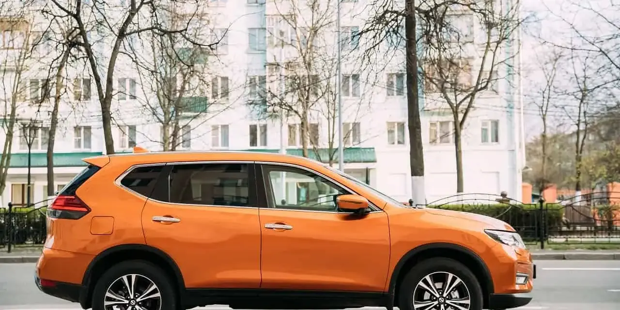 Pomarańczowy SUV do 50 tys. zaparkowany na tle białego budynku i drzew.