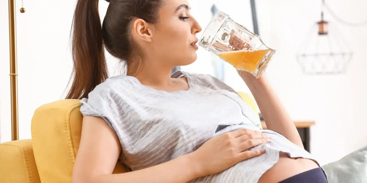 Kobieta w ciąży relaksuje się na kanapie, pijąc piwo bezalkoholowe.