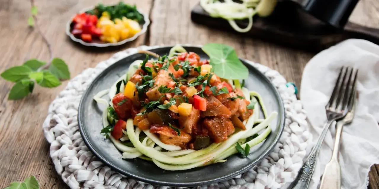 Spaghetti z cukinii z kurczakiem i warzywami w sosie na talerzu.