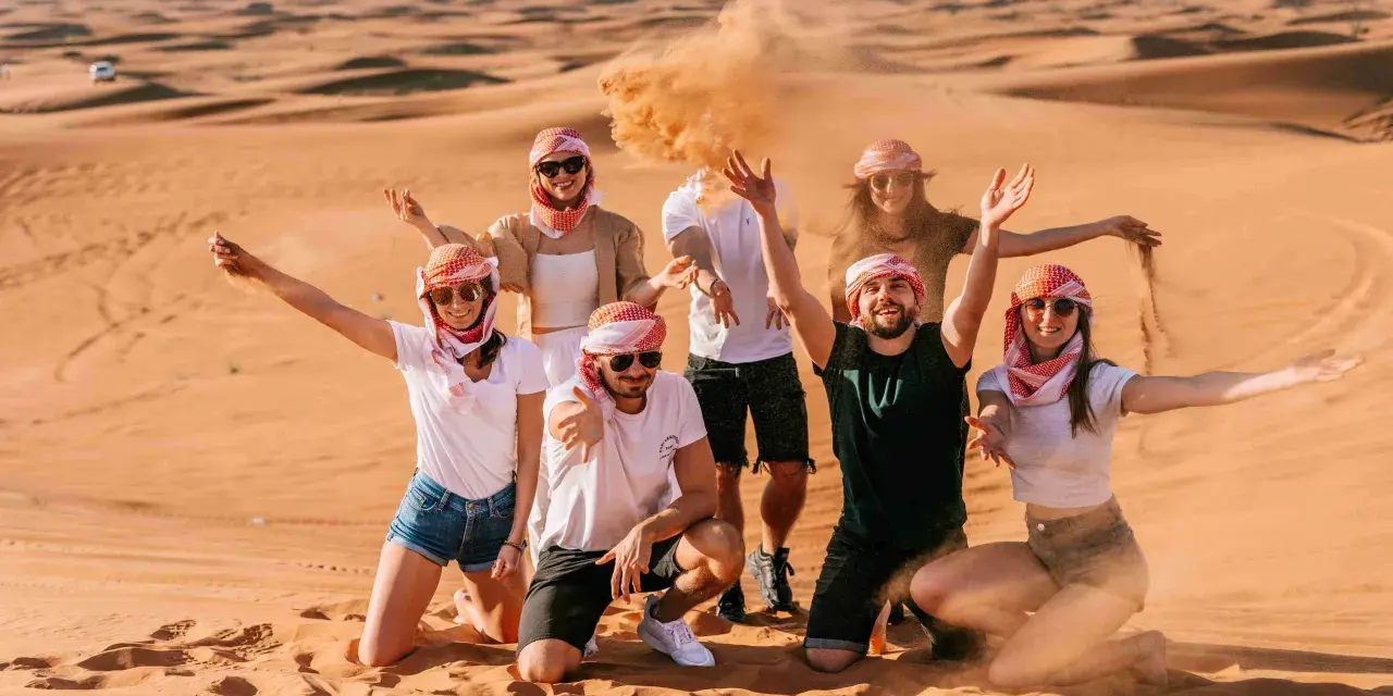 Grupa przyjaciół w tradycyjnych arabskich chustach bawi się piaskiem na pustyni. Wspaniałe wspomnienia z Dubaju w styczniu.