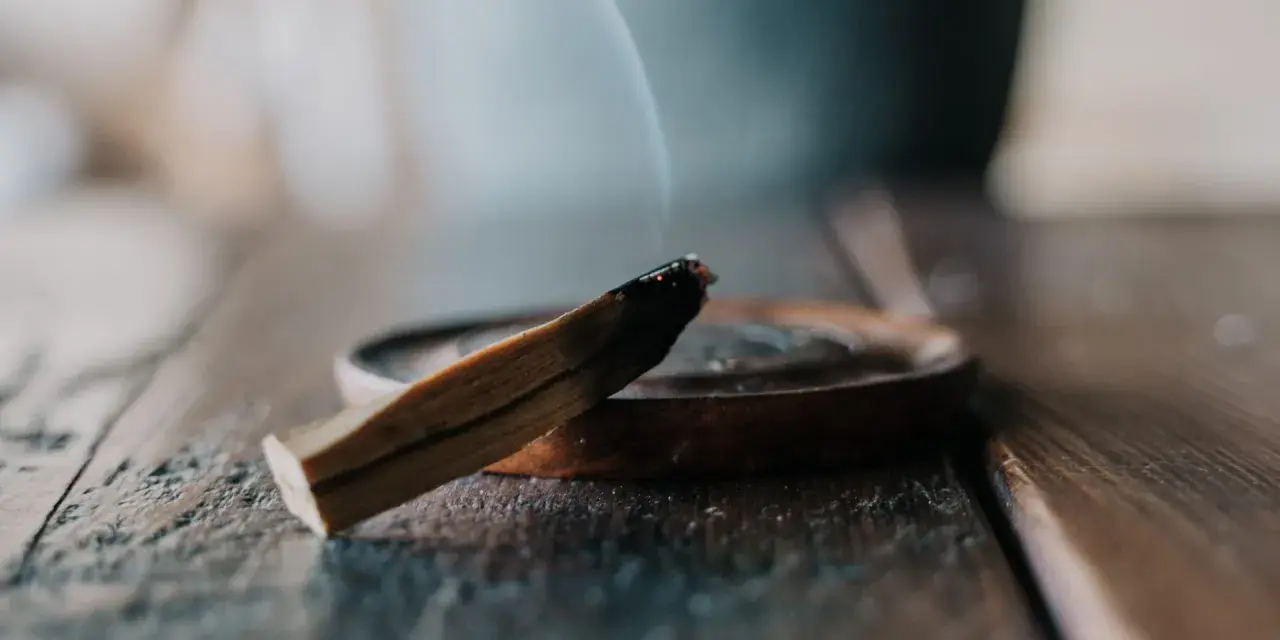 Un palo santo humeante sobre un plato de madera, parte de un ritual de limpieza.