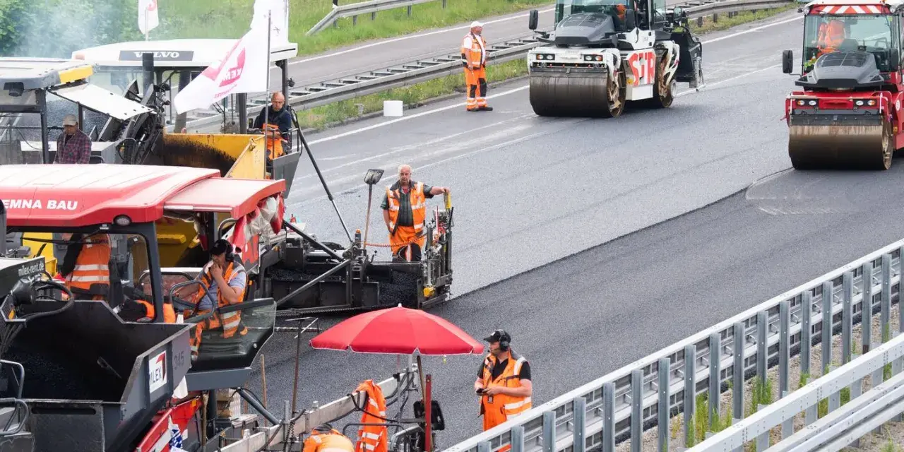 Arbeiter legen auf der ADAC A2 mit Maschinen und Walzen neuen Asphalt.