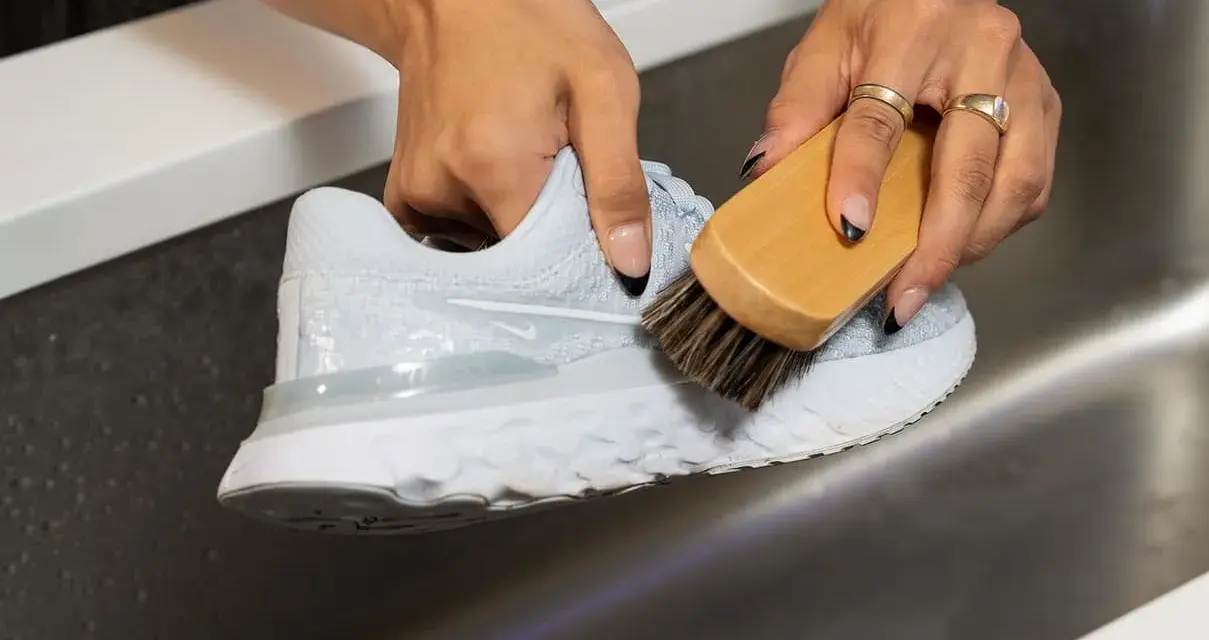 Mani che puliscono una scarpa da ginnastica bianca con una spazzola, mostrando come lavare le tn bianche per farle tornare come nuove.