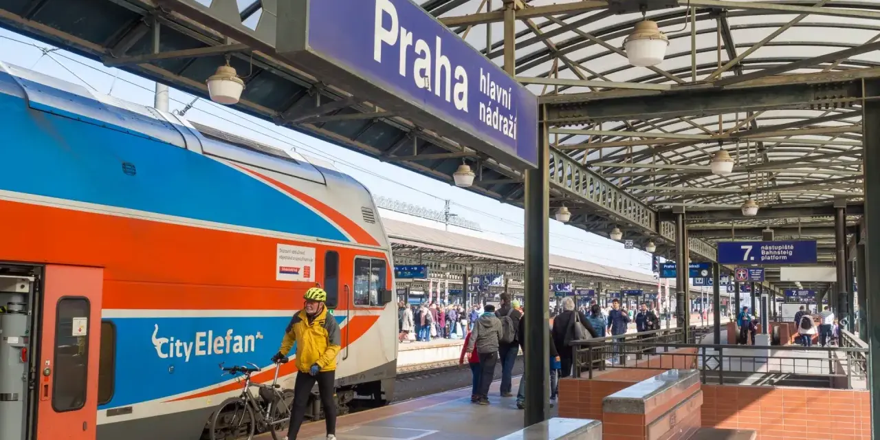 Pociąg z Gdańska do Pragi na dworcu głównym. Mężczyzna w żółtej kurtce z rowerem czeka na peronie.