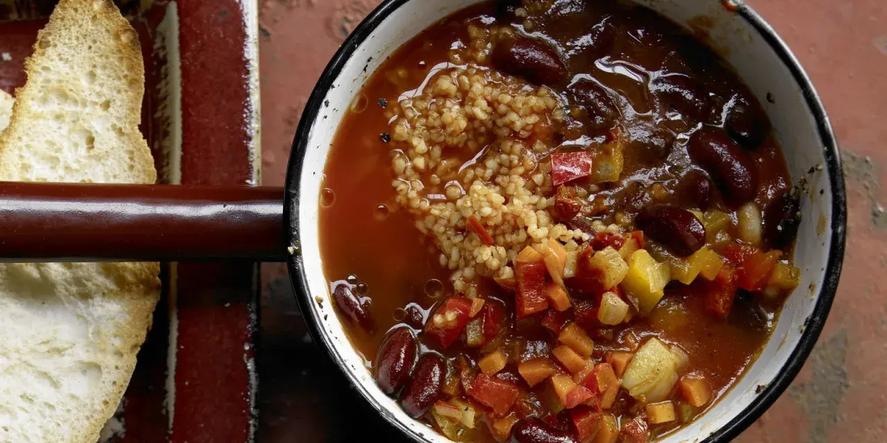 Herzhaftes Chili sin Carne mit Kidneybohnen, Bulgur und Gemüse in einem Topf, daneben geröstetes Brot.