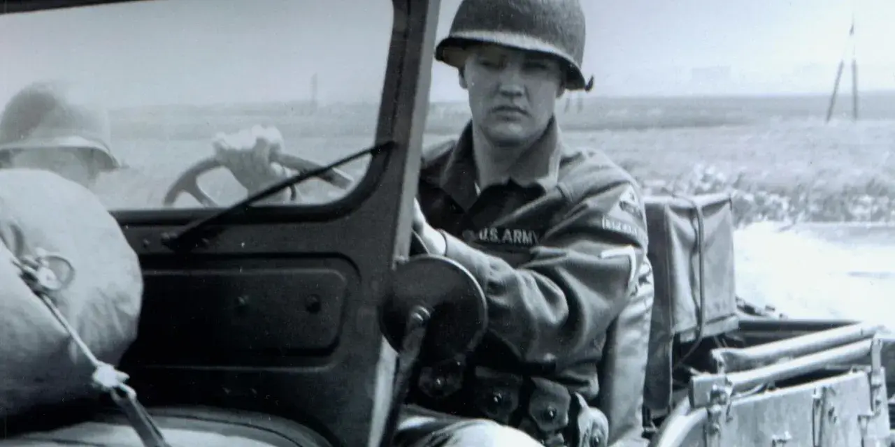 Elvis Presley in seiner US Army Uniform, sitzt am Steuer eines Jeeps.