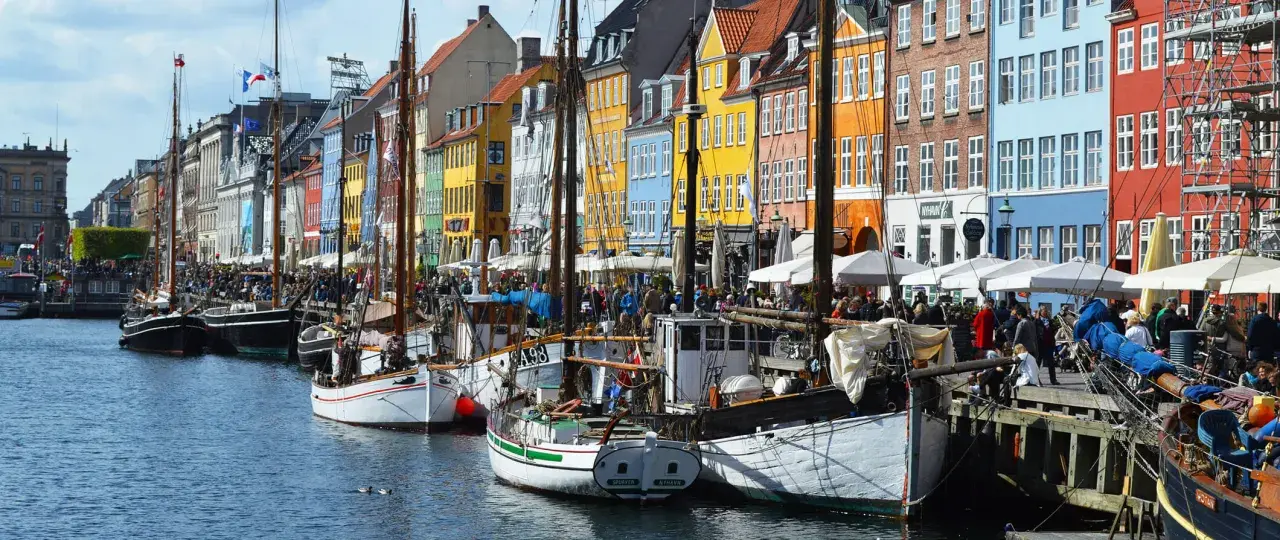 Colorful buildings line a canal in Copenhagen, with boats docked and people enjoying the waterfront. A perfect scene for exploring things to do in Denmark.