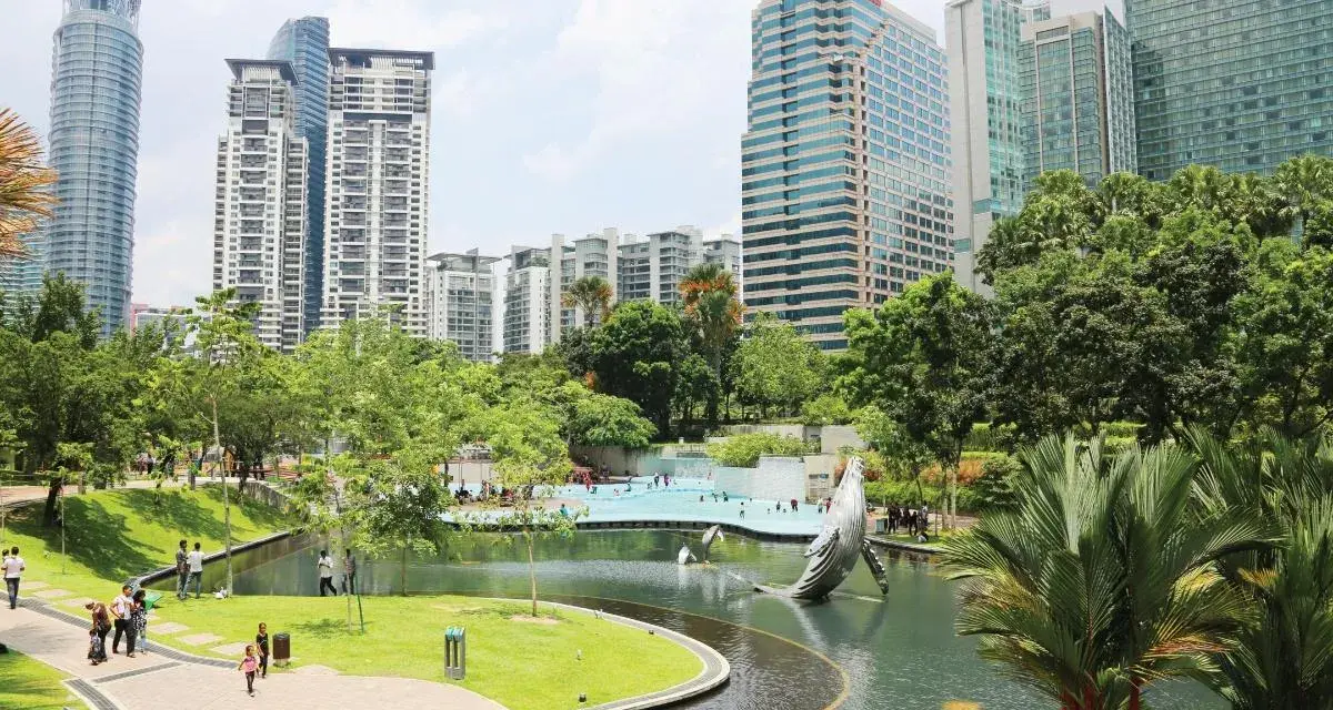 Park z rzeźbą wieloryba i basenem w stolicy Malezji, Kuala Lumpur, otoczony nowoczesnymi wieżowcami.