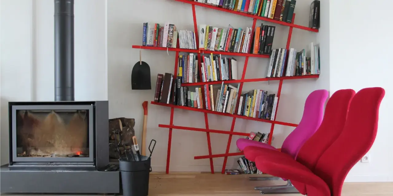 Camino acceso, attrezzi da camino, e moderne piccole librerie rosse piene di libri, con sedie colorate.
