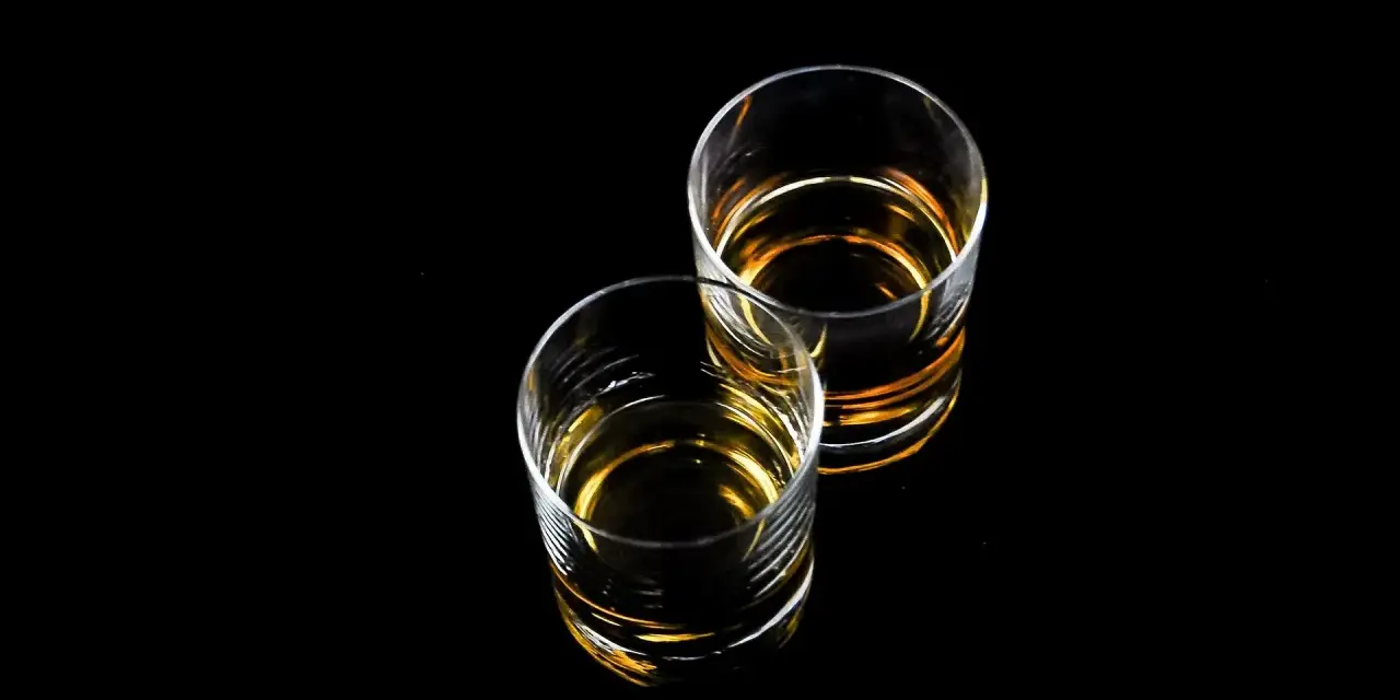 Dwa szklanki z bursztynowym płynem, idealne na wieczór z drinkiem. Czy to Baileys?