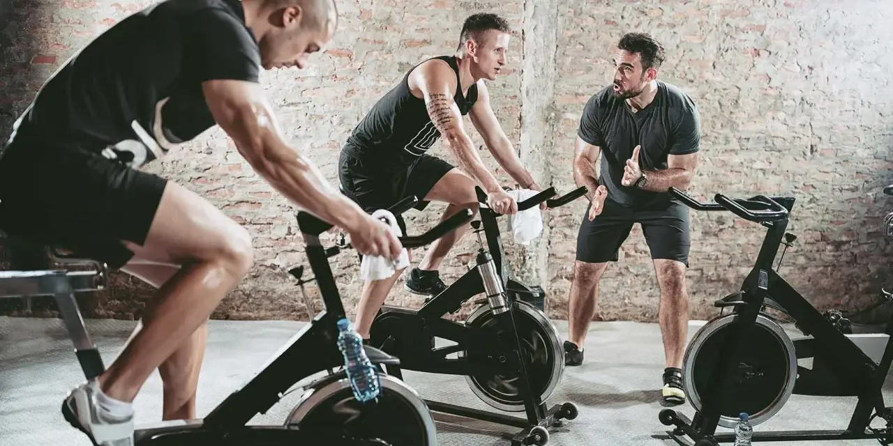 Trainer instructs men on stationary bikes. This workout can help build endurance, proving a stationary bike helps with running.