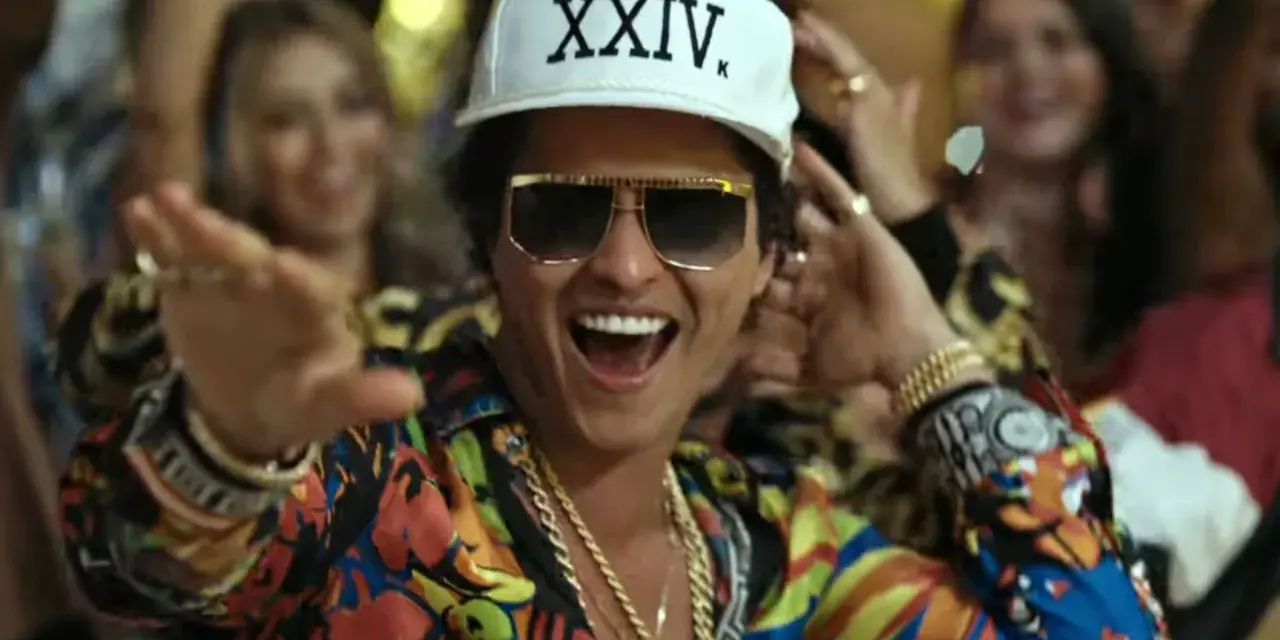 Bruno Mars w Polsce! Wesoły artysta w kolorowej koszuli i czapce z napisem "XXIV K" tańczy wśród rozbawionych ludzi.