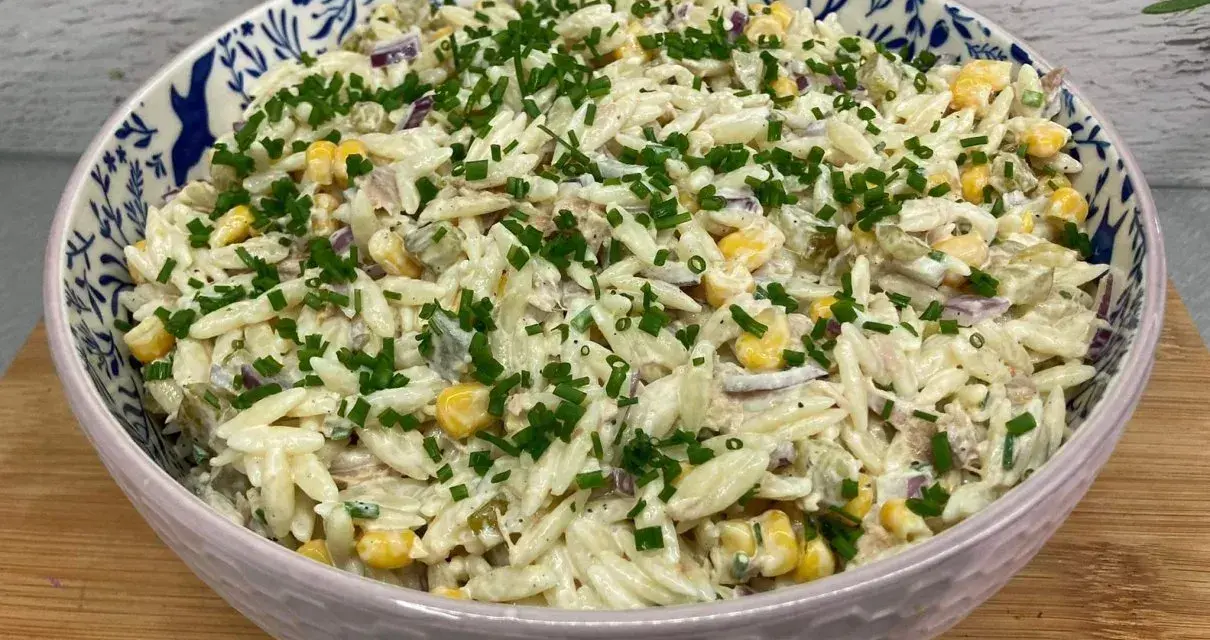 Pyszna sałatka z tuńczykiem, makaronem orzo, kukurydzą i szczypiorkiem, podana w ozdobnej misce.