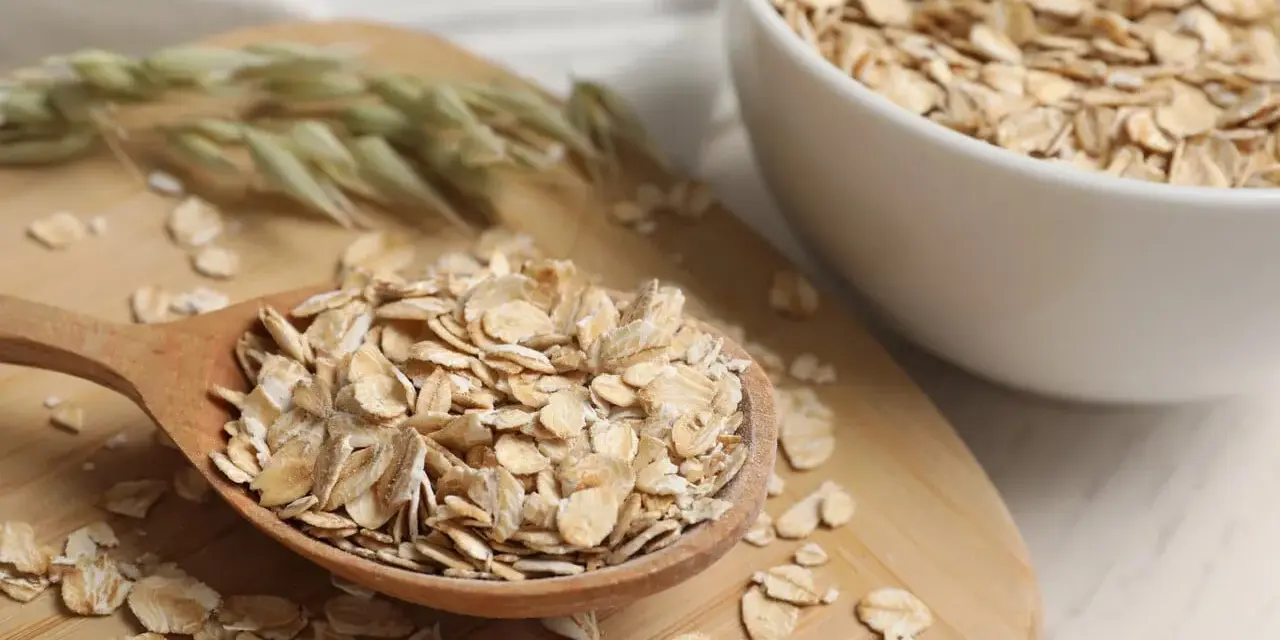 Płatki owsiane na drewnianej łyżce i w misce. Czy płatki owsiane mają gluten? Czysty owies jest bezglutenowy, ale warto sprawdzić etykietę.