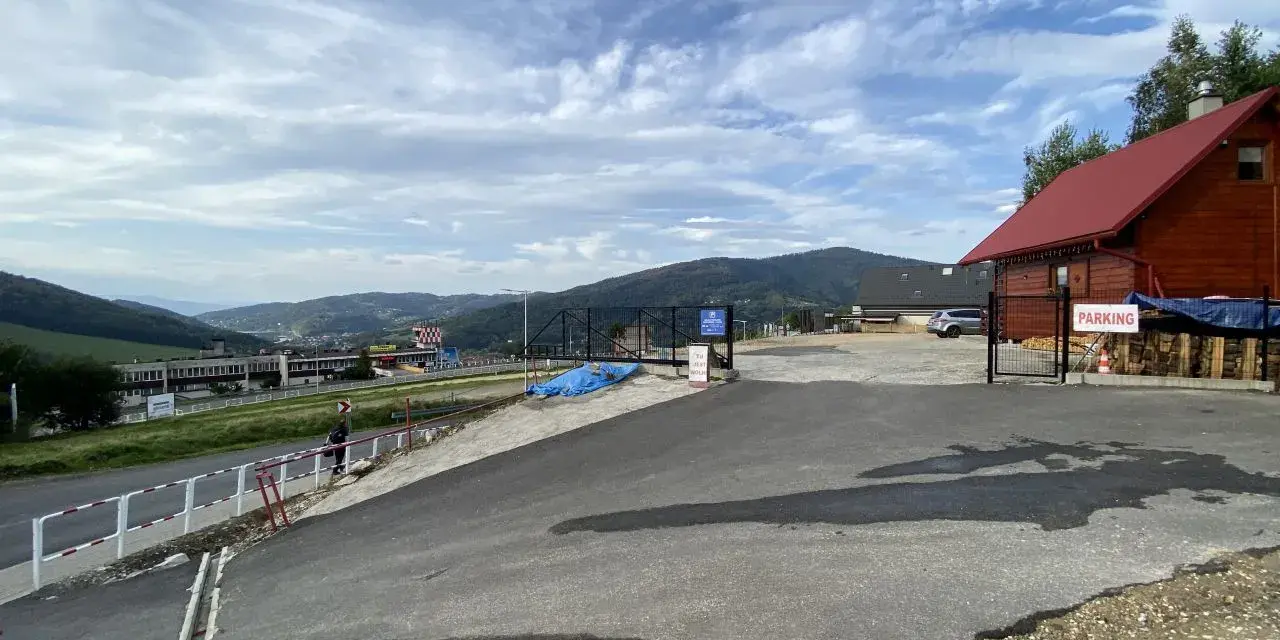 Widok na parking przy górze Żar. W oddali widać zabudowania i góry.
