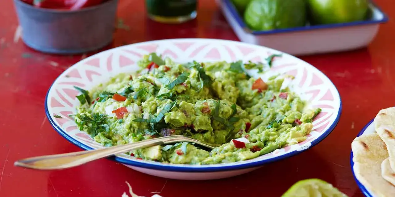 En skål med krämig guacamole, perfekt för ditt nästa guacamole recept. Serveras med tortillabröd, lime och chili.