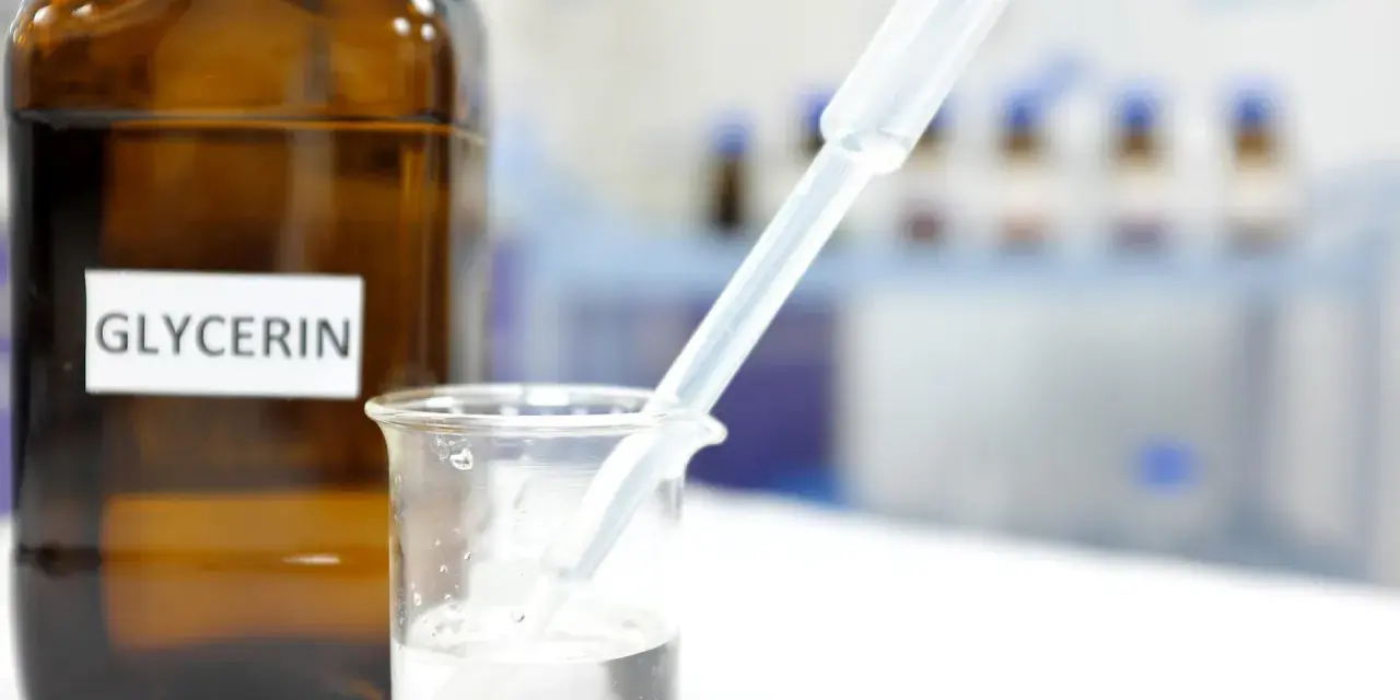 Braunglasflasche mit der Aufschrift "Glycerin". Ein Pipette tropft in ein Becherglas mit klarer Flüssigkeit, was die Glycerin verwendung in der Forschung zeigt.