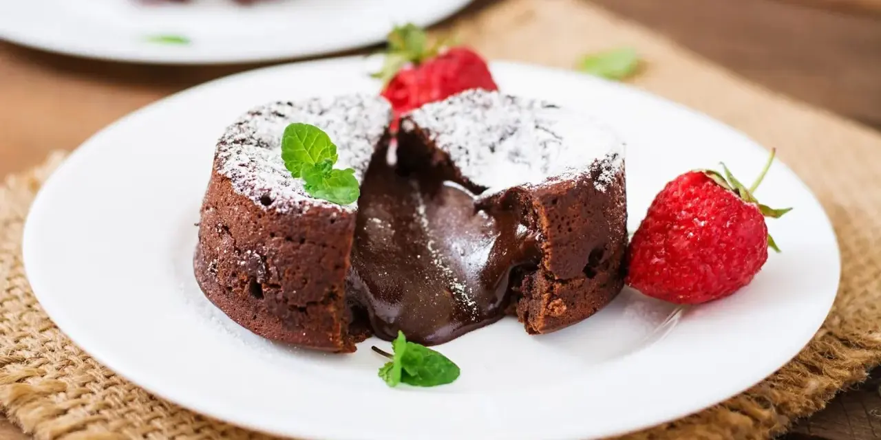 Pyszny fondant czekoladowy z płynnym środkiem, przypominający małe soufflé czekoladowe, podany z truskawkami i miętą.