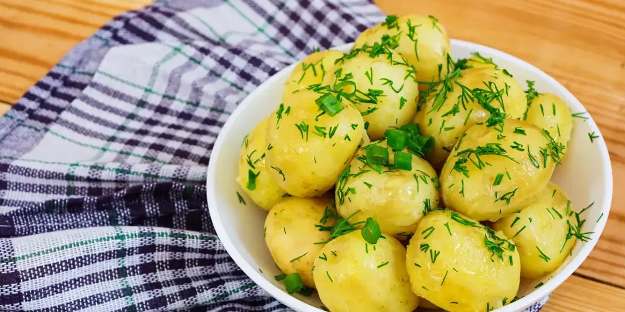 Młode ziemniaki w misce, posypane koperkiem i szczypiorkiem. Idealne na lato, a ile gotować młode ziemniaki? Krótko!