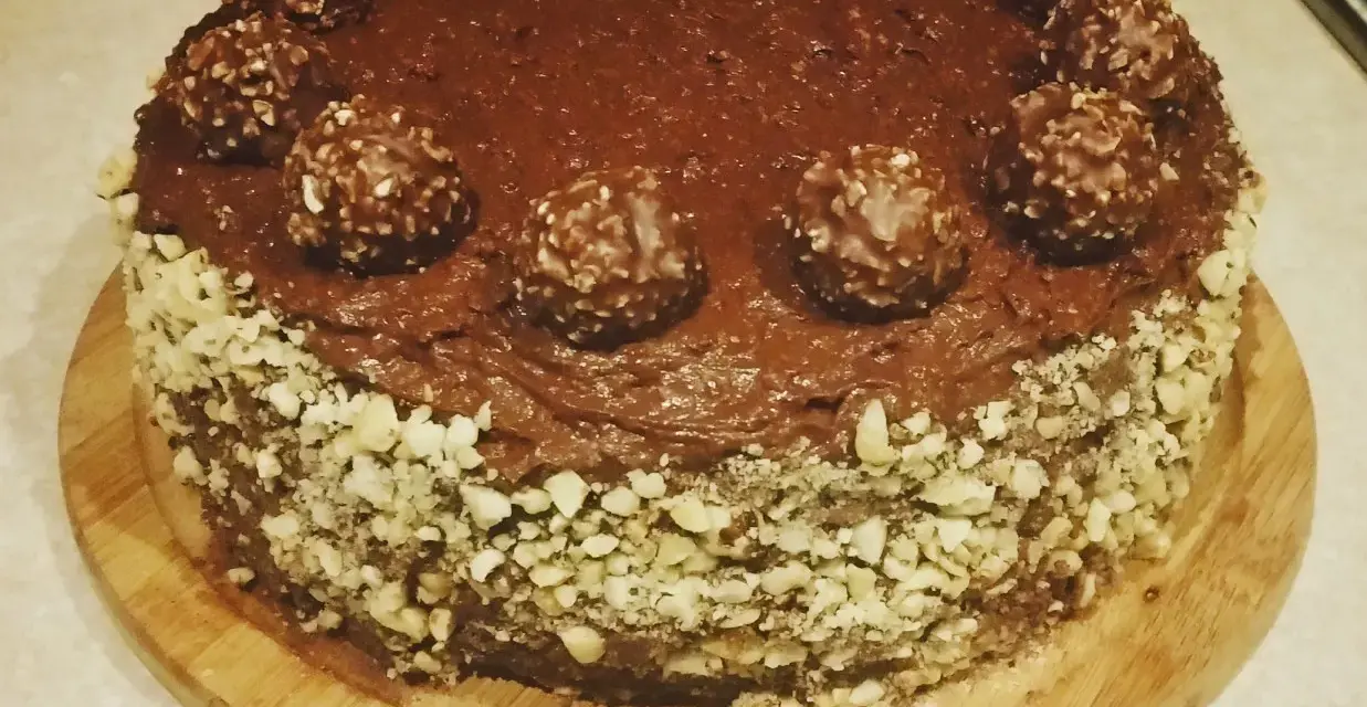 Pyszny tort ferrero rocher, oblany czekoladą i ozdobiony orzechami oraz kulkami.