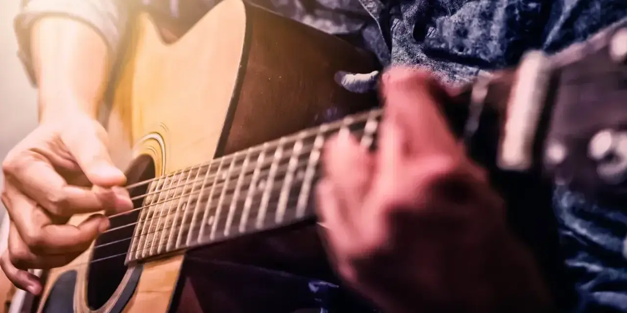 Ręce grające na gitarze akustycznej. Idealne dla tych, którzy zaczynają swoją przygodę z nauką gry na gitarze dla początkujących.