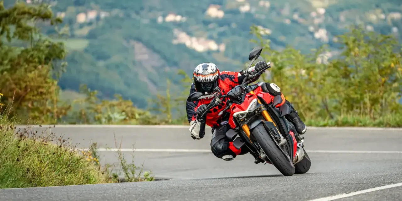 Un motociclista esperto piega in una curva stretta, con il ginocchio quasi a terra, affrontando un passo in montagna.