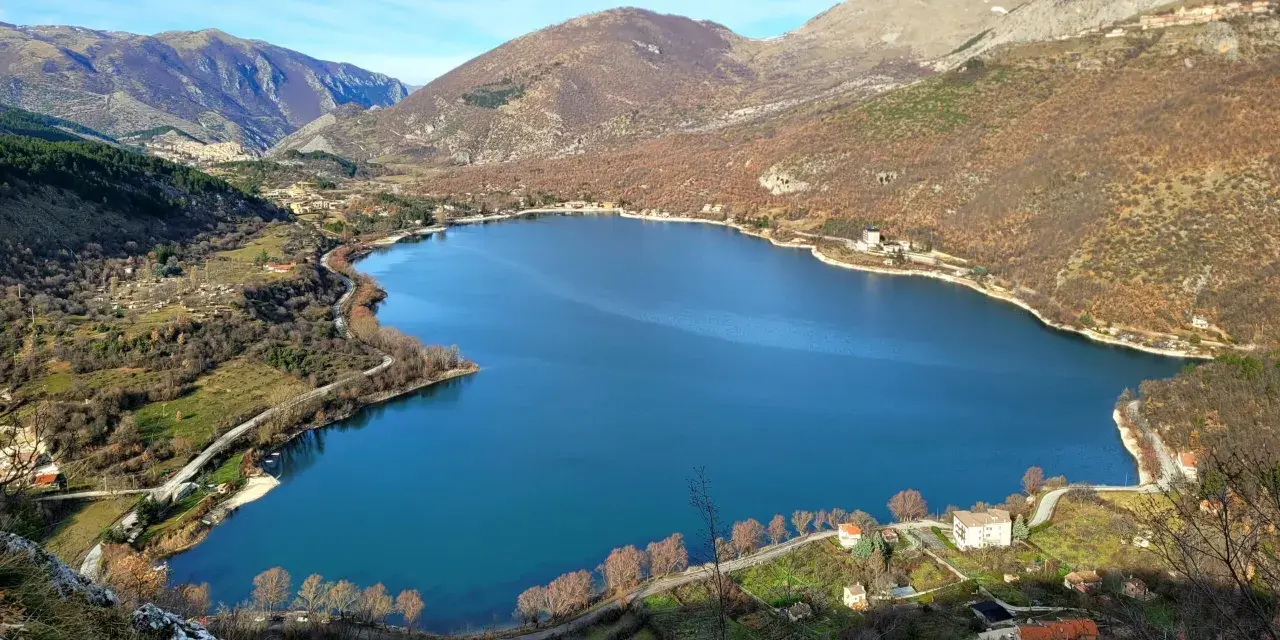 Panoramica del lago di Scanno, con montagne sullo sfondo e case sparse lungo la riva. Un luogo incantevole da esplorare.