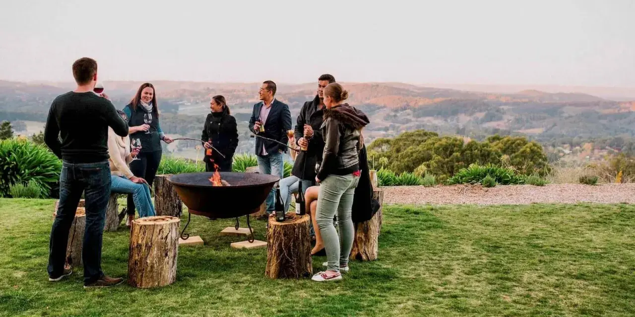 Staff retreat ideas for nonprofits: A group enjoys a bonfire and drinks outdoors, surrounded by rolling hills.