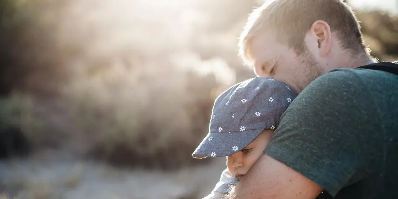 Ojciec mocno tuli dziecko w czapce z kwiatkami. To piękny moment, który pokazuje, jak ważny jest **asperger przytulanie** dla budowania więzi i poczucia bezpieczeństwa.