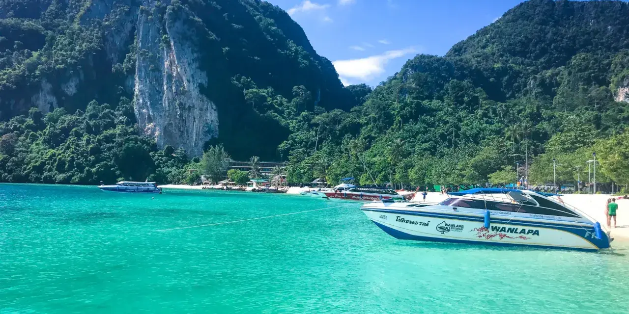 Turkusowa woda i łodzie motorowe przy plaży w Maya Bay. W tle zielone, skaliste góry.