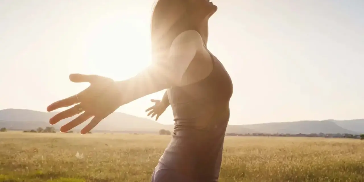 Frau mit ausgebreiteten Armen im Sonnenlicht, ein Symbol für das Heilen von Hypochondrie und das Finden von innerem Frieden.