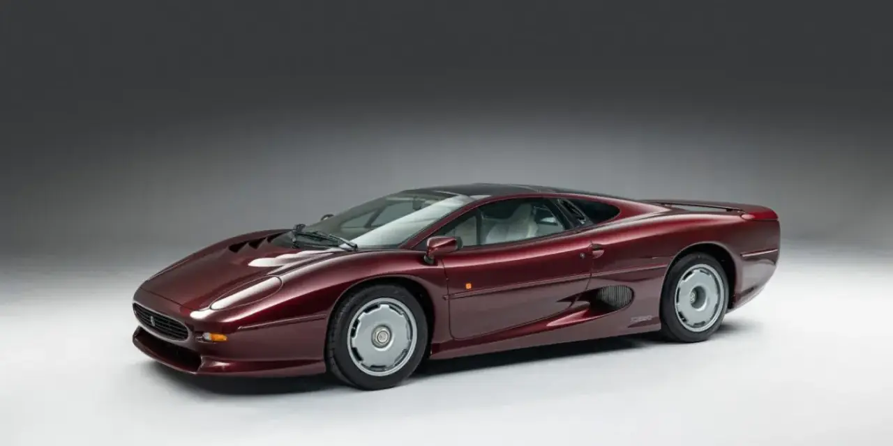 Bordowy Jaguar XJ220, ikona motoryzacji lat 90., prezentuje swoje aerodynamiczne linie na tle szarego tła.