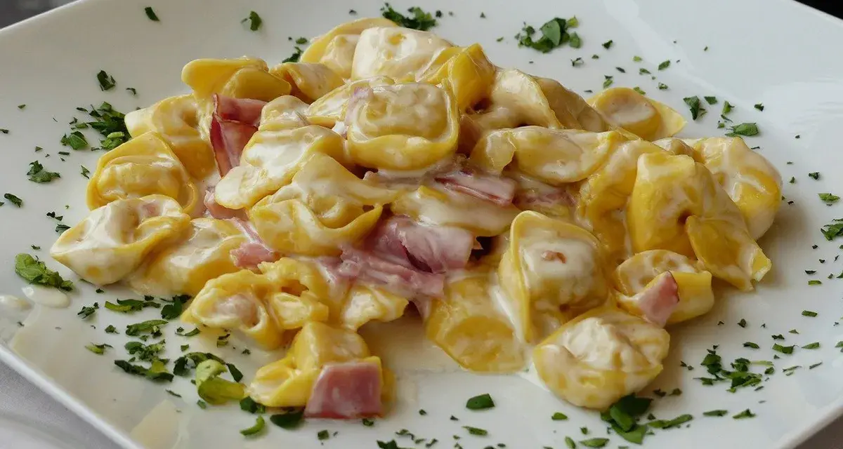 Tortellini panna e prosciutto, un classico piatto italiano, serviti su un piatto bianco con prezzemolo tritato.