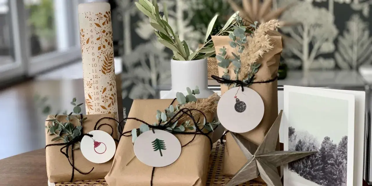 Schöne Geschenk verpacken Ideen: Geschenke in braunes Papier, mit Zweigen und Anhängern dekoriert, neben einer Adventskerze und einer Weihnachtskarte.