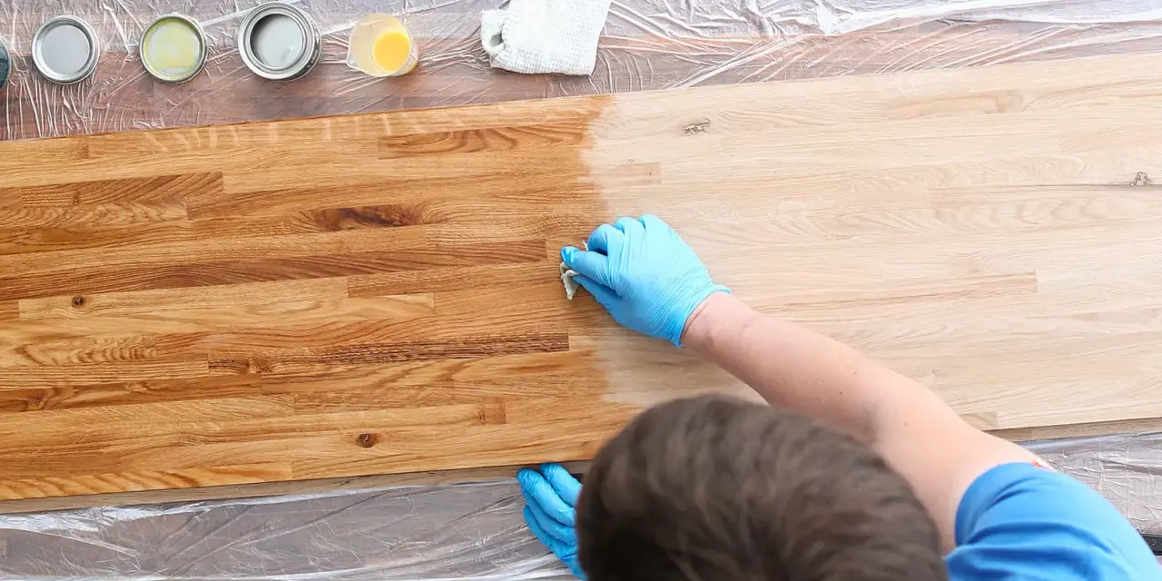 Mani guantate applicano un trattamento per come indurire il legno. Tavolo in legno con diverse lattine di finitura.