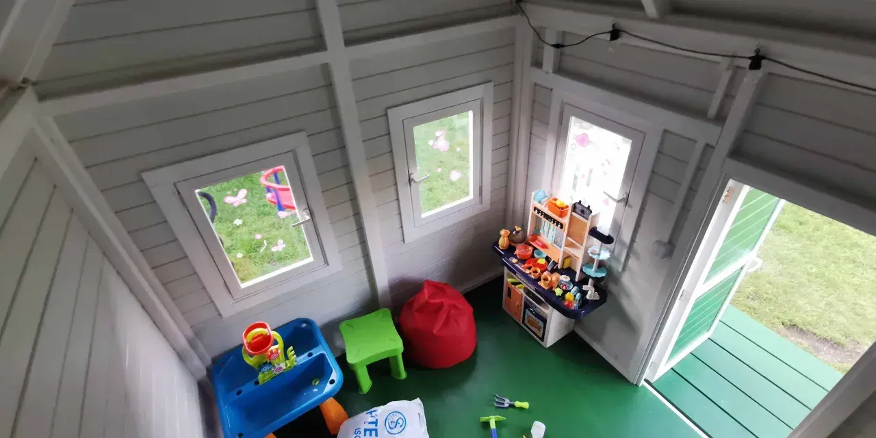 Jak urządzić domek dla dzieci w środku? Zabawki, stolik, kuchnia i pufy tworzą przytulną przestrzeń do zabawy.